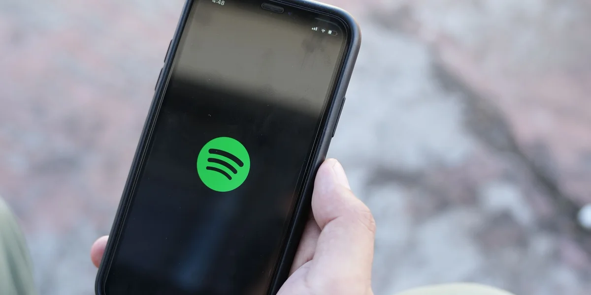 A person's hand holding a phone where Spotify app is getting opened.